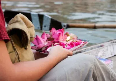 Person holding a plate with pink flowers and candles in a boat on a river